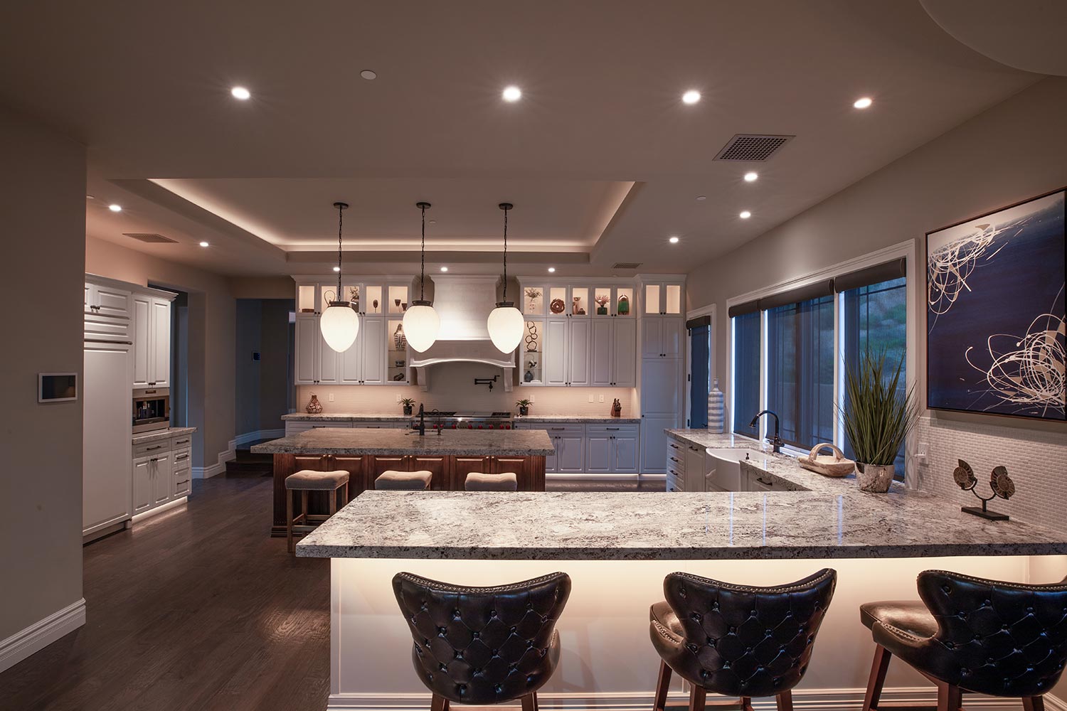 A modern kitchen featuring pendant lights, granite countertops, dark wood floors, and white cabinets.