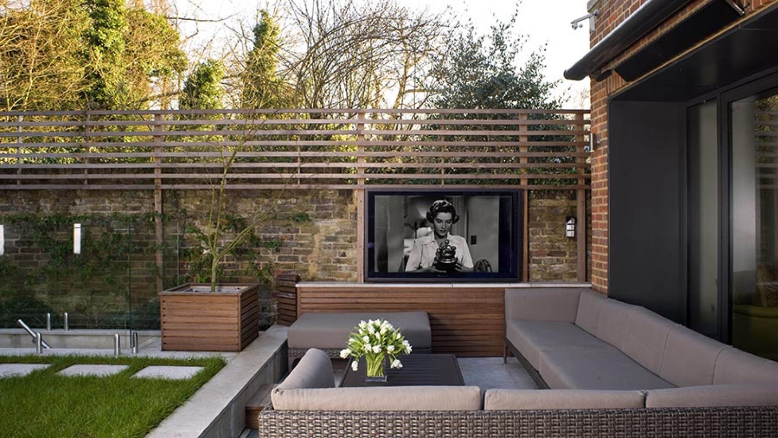 A stylish outdoor patio with a TV displaying a black-and-white movie, surrounded by a comfortable seating area.
