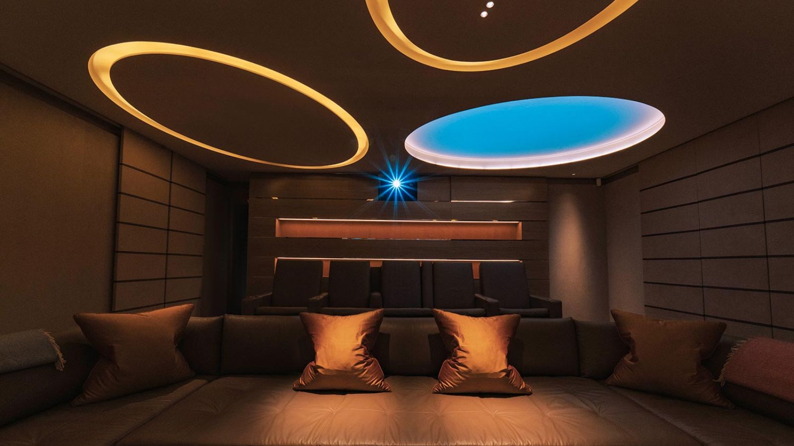 Luxurious theater with ambient lighting, soft seating, and a glowing blue projector on the ceiling.