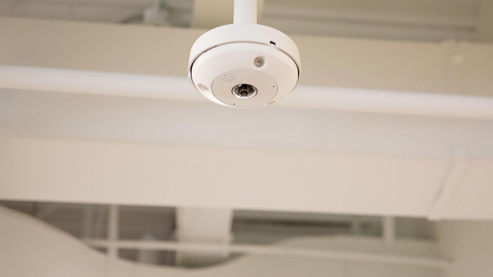 White ceiling-mounted indoor security camera in a modern building.