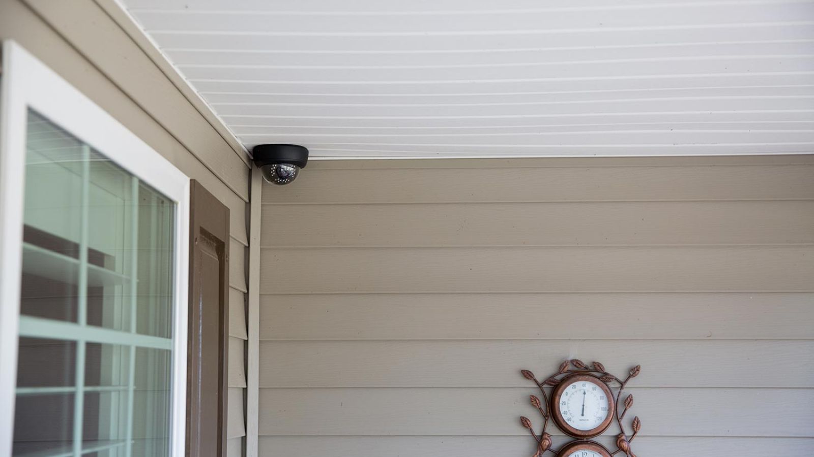 Black dome security camera mounted on a porch ceiling, with decorative wall clocks nearby.