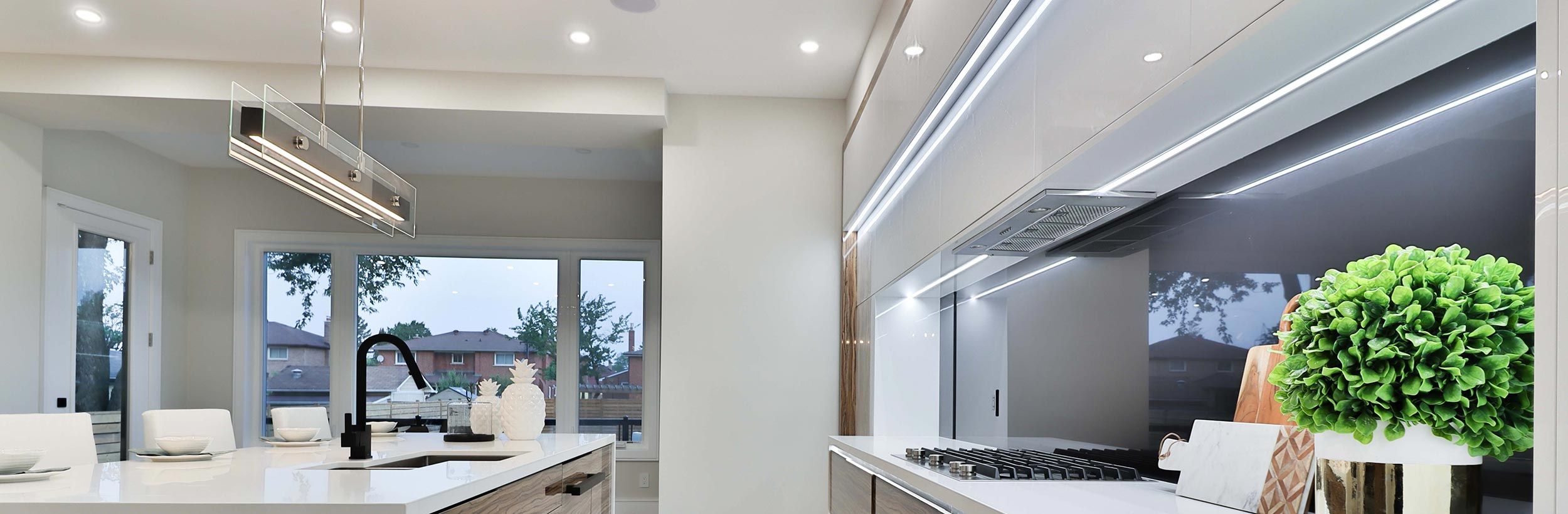 Contemporary kitchen with linear LED lighting, white countertops, and large windows.