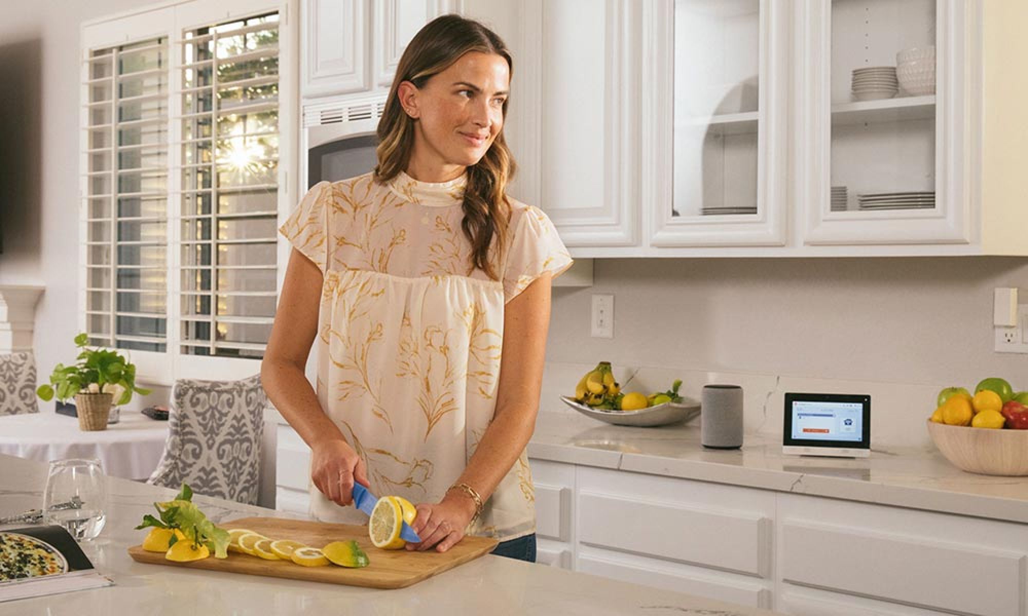 A woman preparing food in a modern kitchen while interacting with a sleek smart display on the countertop.