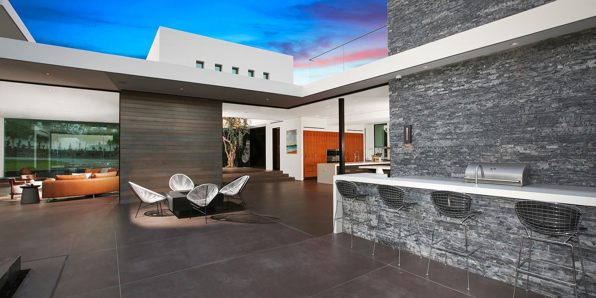 A sleek modern outdoor kitchen with bar seating, adjacent to a contemporary living area and patio.