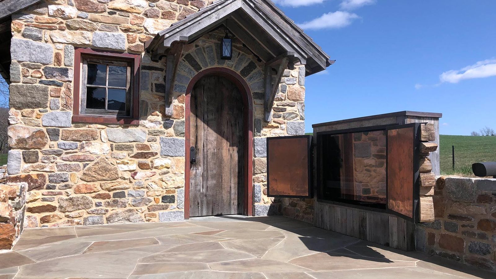 Stone patio area with a rustic small building and a wooden door.