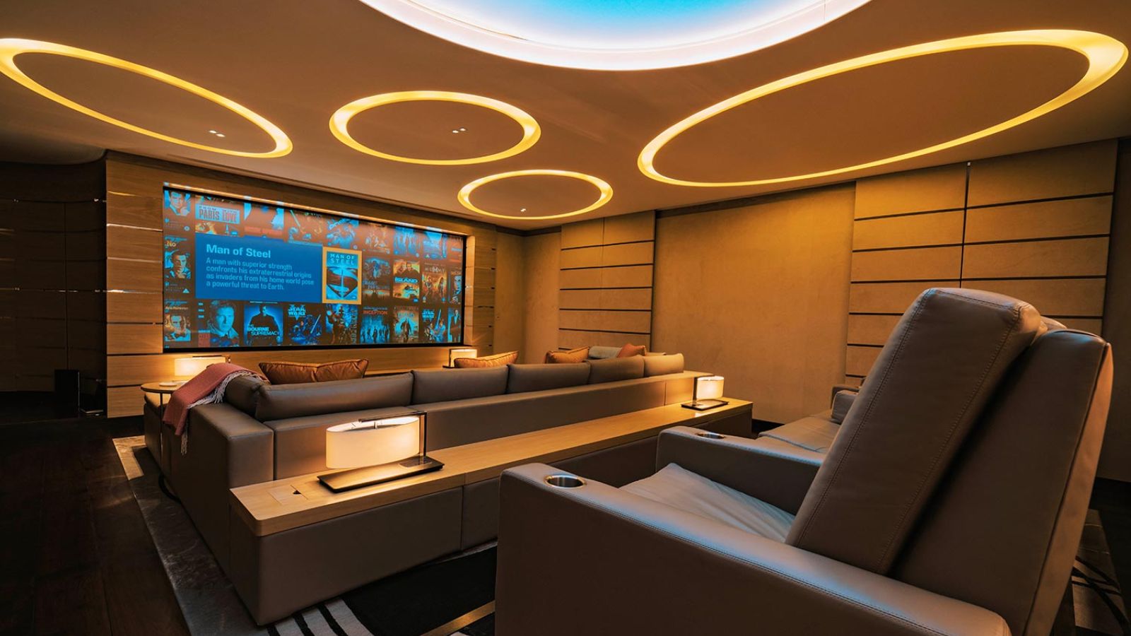 Warm home cinema with layered seating, glowing circular lights, and a movie menu on display.