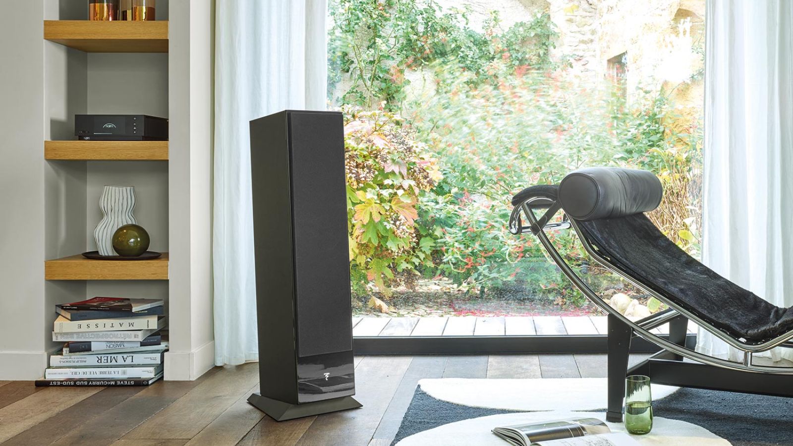 Cozy corner with a black speaker, bookshelves, and a reclining chair next to a large window.