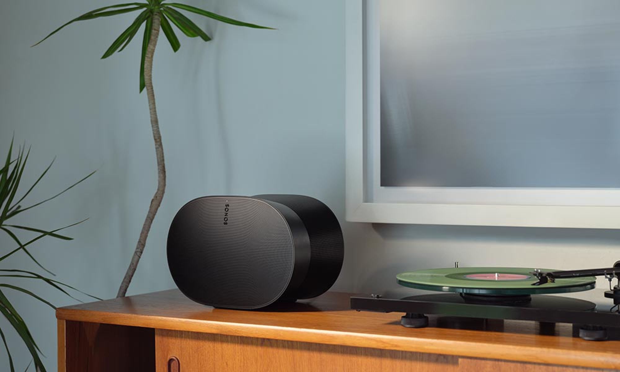 A modern speaker placed on a vintage wooden cabinet next to a turntable and vinyl record.